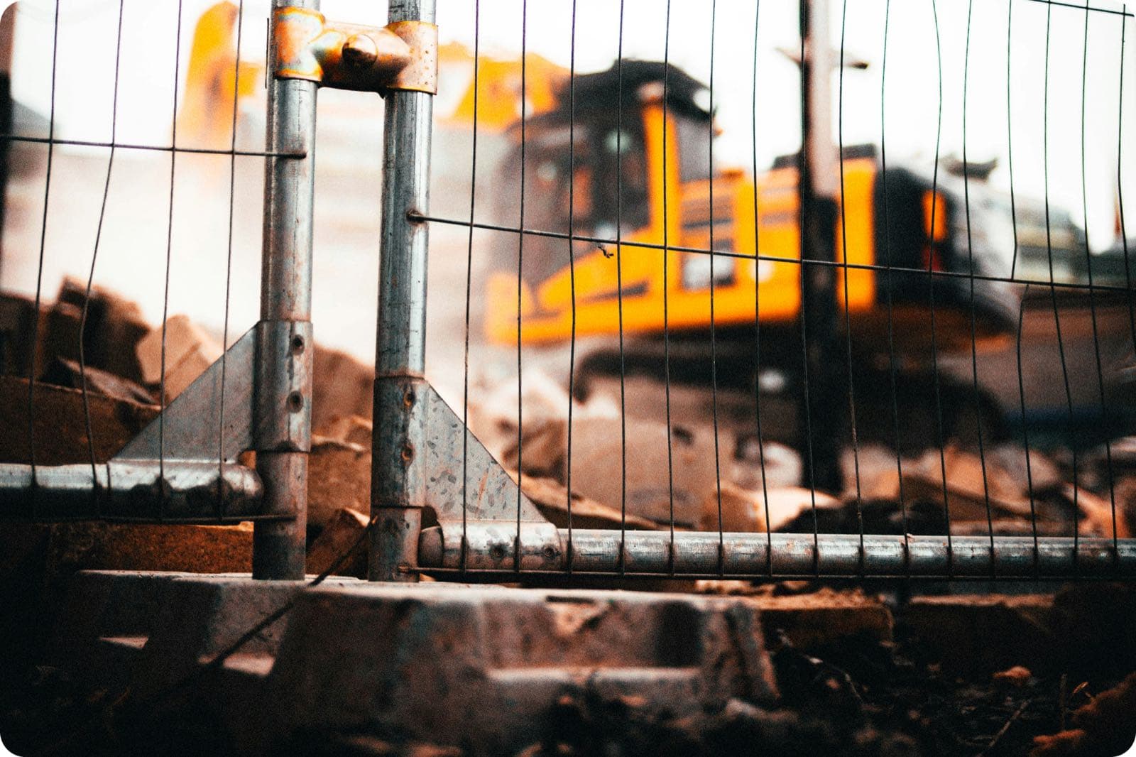 A construction site behind a chain-link fence with a yellow bulldozer and demolition debris, the kind of jobsite that isn't on any map yet