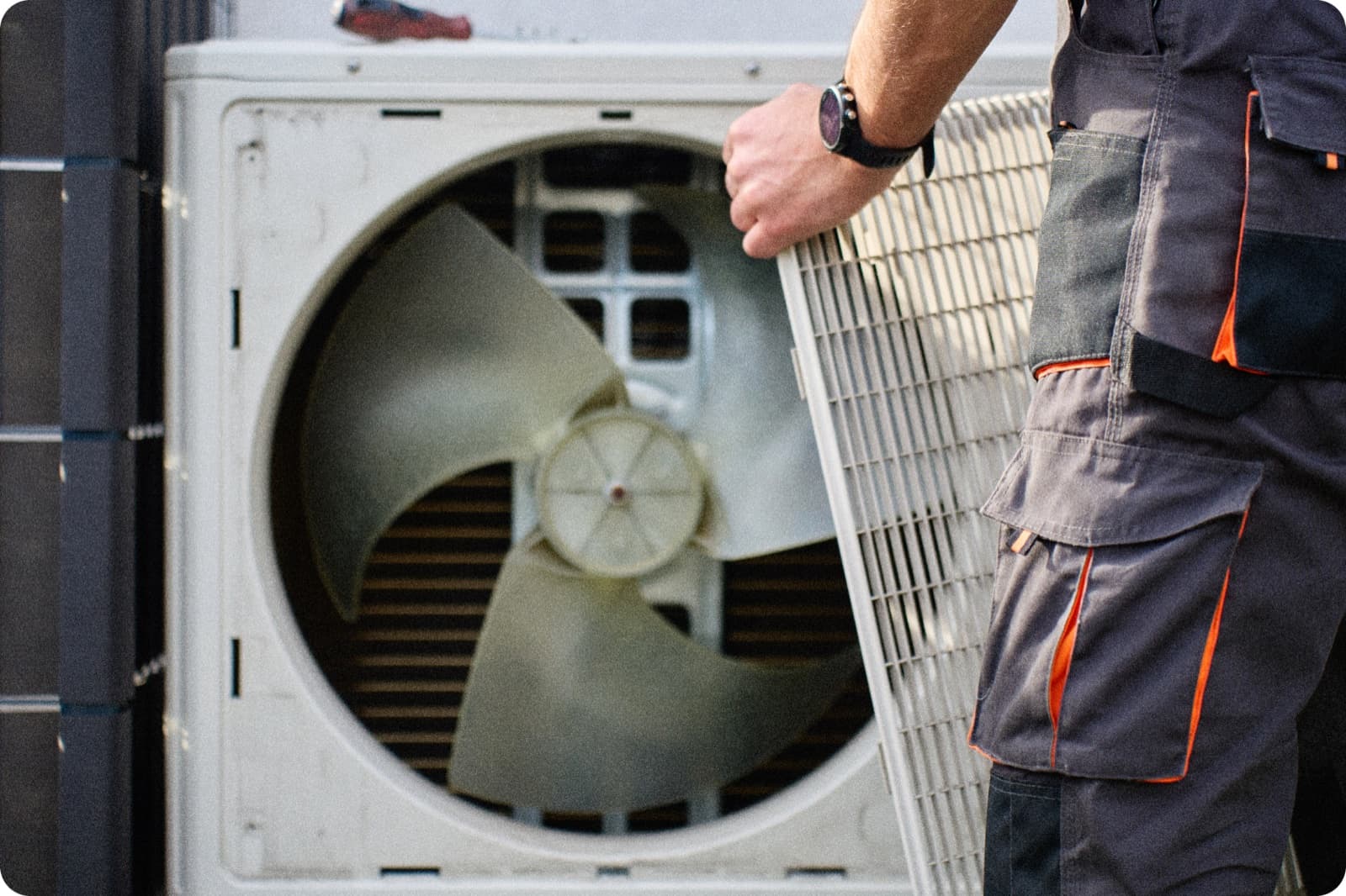 HVAC technician in work uniform removing the cover panel from an outdoor air conditioning unit