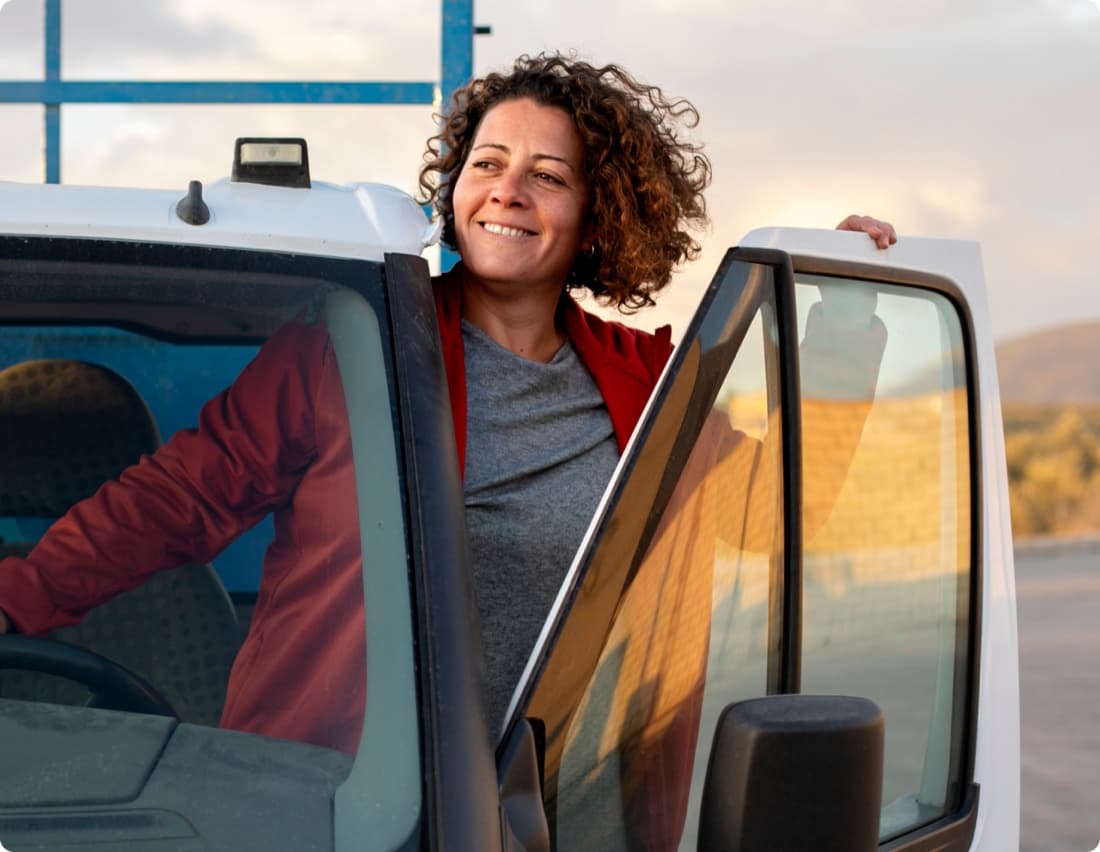 Curri Dedicated Routes driver in a red jacket stepping out of her pickup truck at golden hour — insured, trained, and background-checked local driver scheduled for the full day