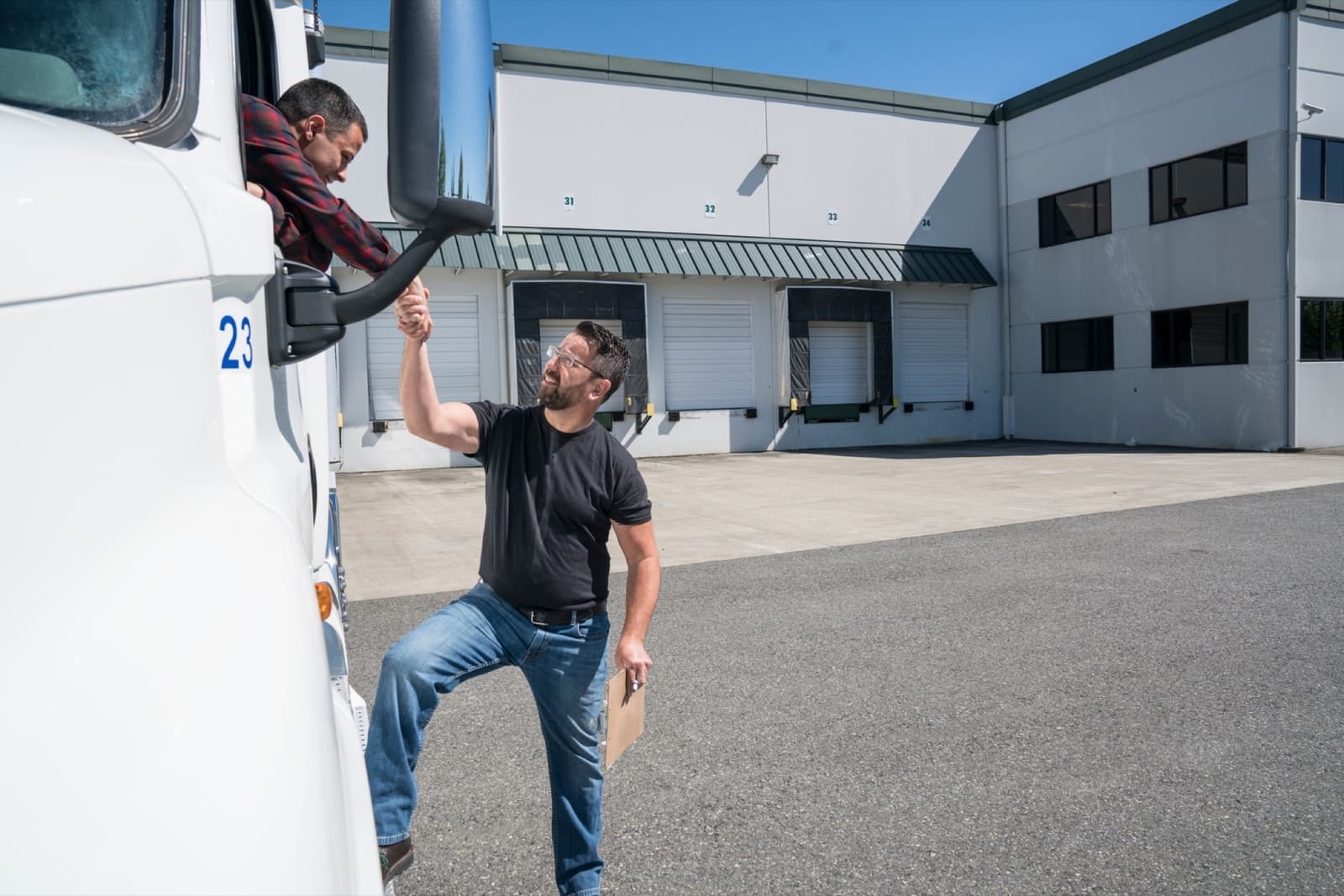 Curri Dedicated Routes driver in a red jacket loading a pickup truck at a distribution warehouse bay 23 — reliable local drivers handling recurring milk runs, FTL, and LTL deliveries