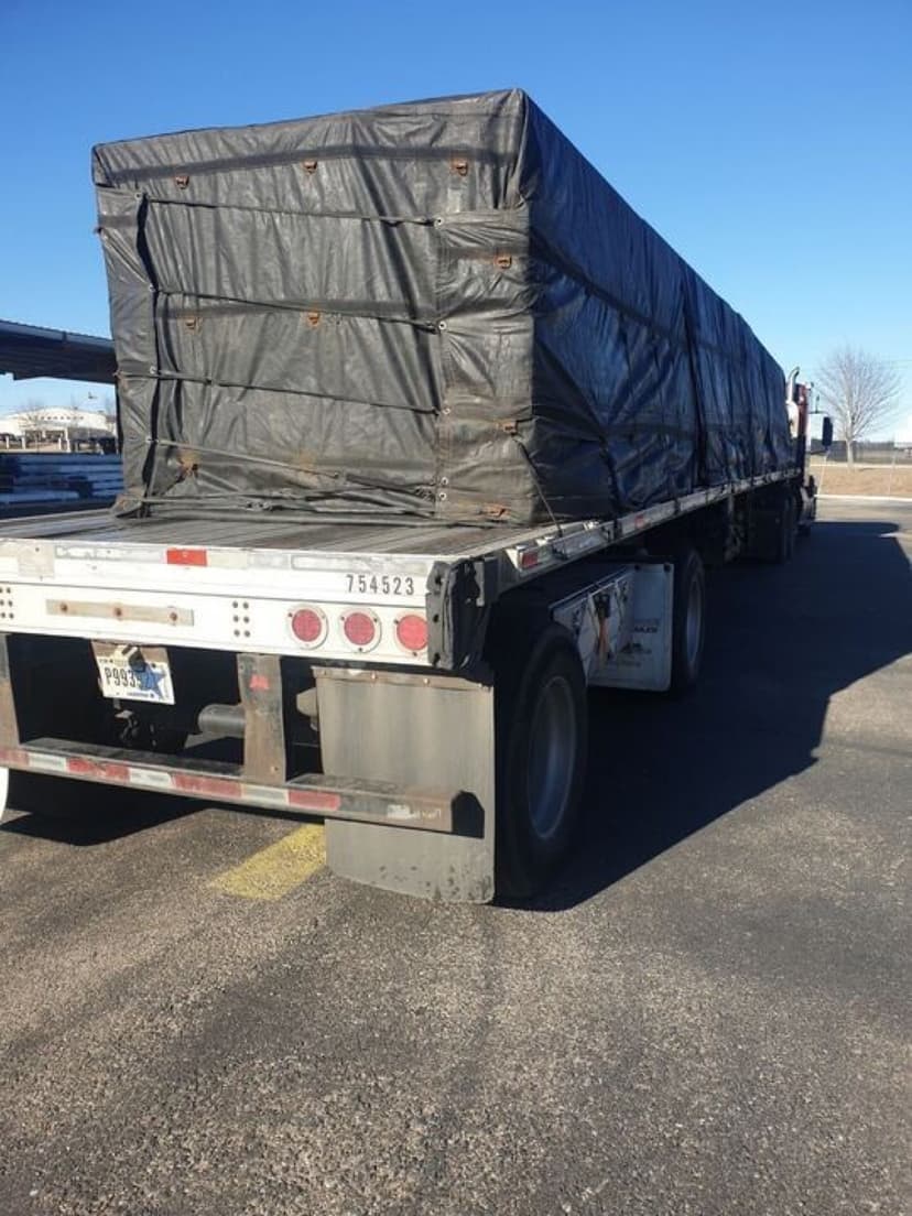 Tarped flatbed load strapped to a Curri semi for a long-haul jobsite delivery of construction materials
