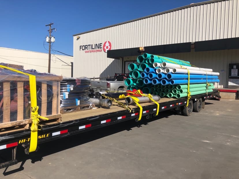 Flatbed loaded with bundles of colorful PVC pipe at a Fortiline supply yard for a Curri plumbing-supply pickup