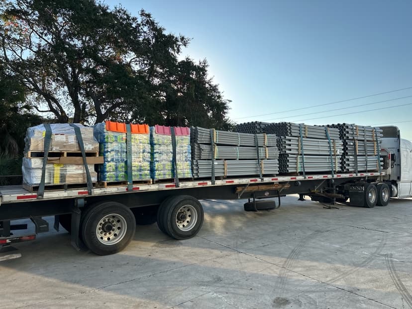 Flatbed semi loaded with grey conduit and palletized fittings for a Curri electrical-supply distribution run