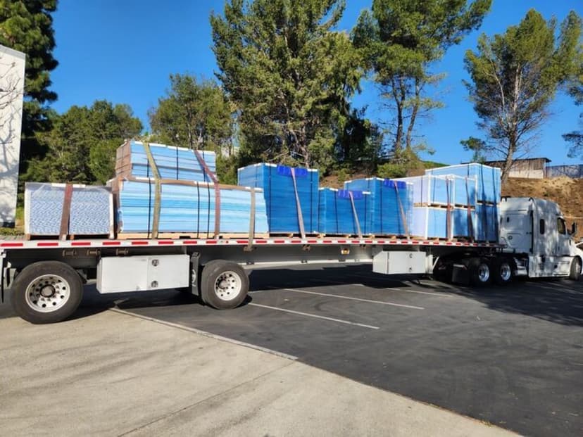 Flatbed semi loaded with stacked blue insulation panels for a Curri building-materials delivery to a jobsite