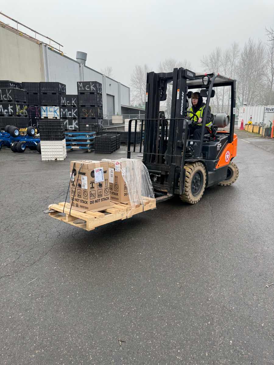 Forklift operator in hi-vis lifting crated cargo at a Curri Moffett delivery jobsite