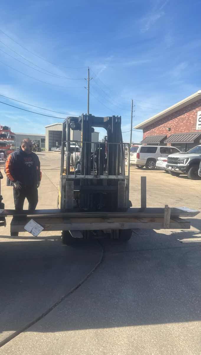 Yellow forklift with extended forks ready to unload a Curri Moffett delivery while the operator stages the load