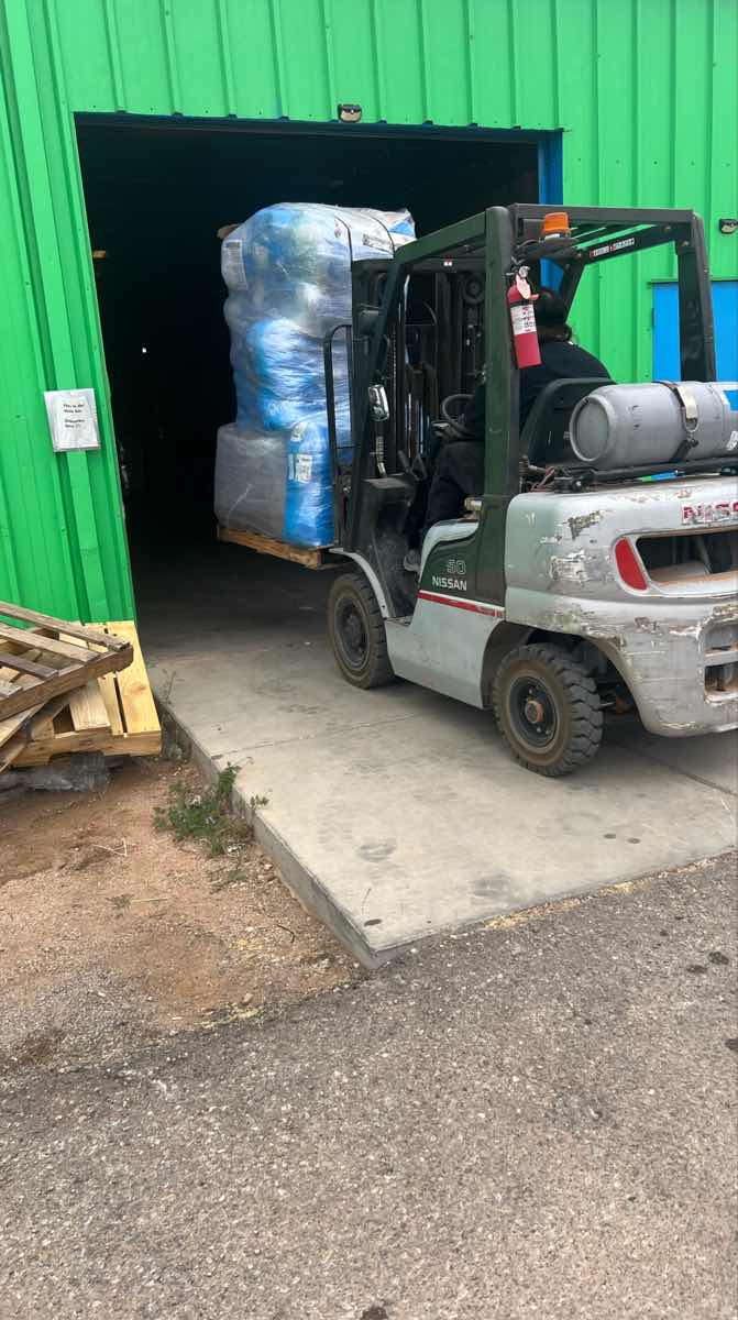 Nissan forklift carrying a blue-wrapped pallet into a warehouse on a Curri Moffett-equipped run