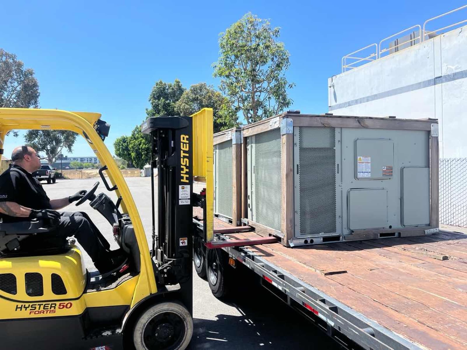 Yellow Hyster forklift loading an HVAC unit onto a Curri flatbed for a same-day Moffett delivery to a jobsite