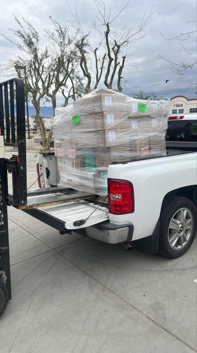 Forklift loading a shrink-wrapped pallet into the bed of a white pickup truck for a Curri trade-supply pickup