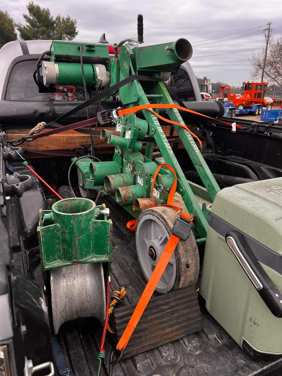 Pickup truck bed loaded with green plumbing equipment and conduit strapped down for a Curri trade delivery