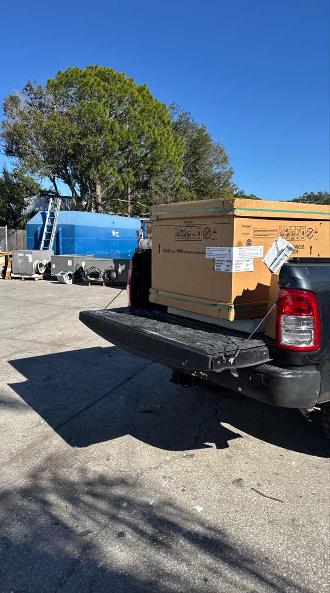 Black pickup truck with the tailgate down and a large appliance carton loaded for a Curri big-box retail delivery