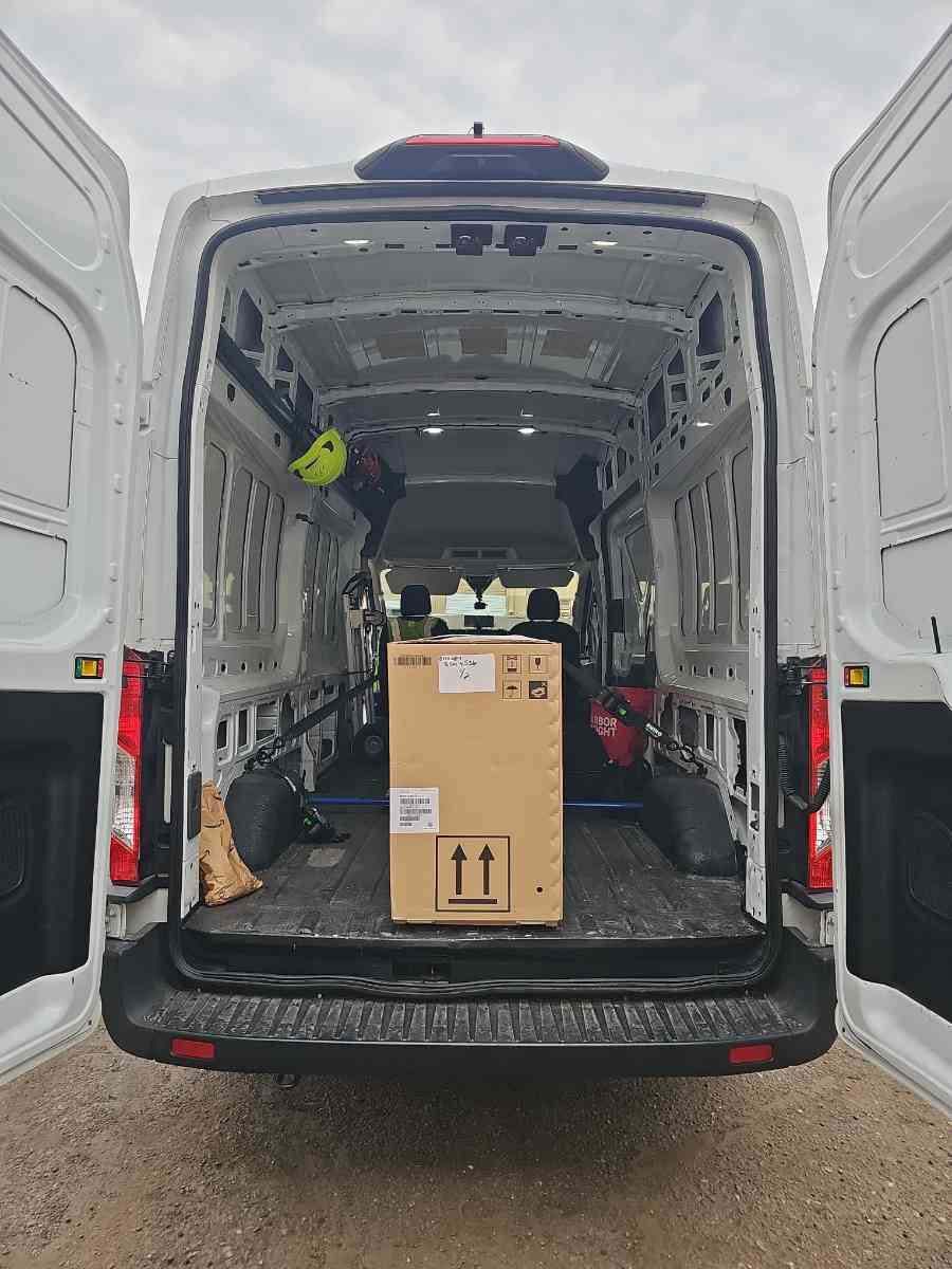 Rear of a high-roof Curri Sprinter Van with the doors open and a large cardboard box loaded inside, ready for a same-day enclosed delivery