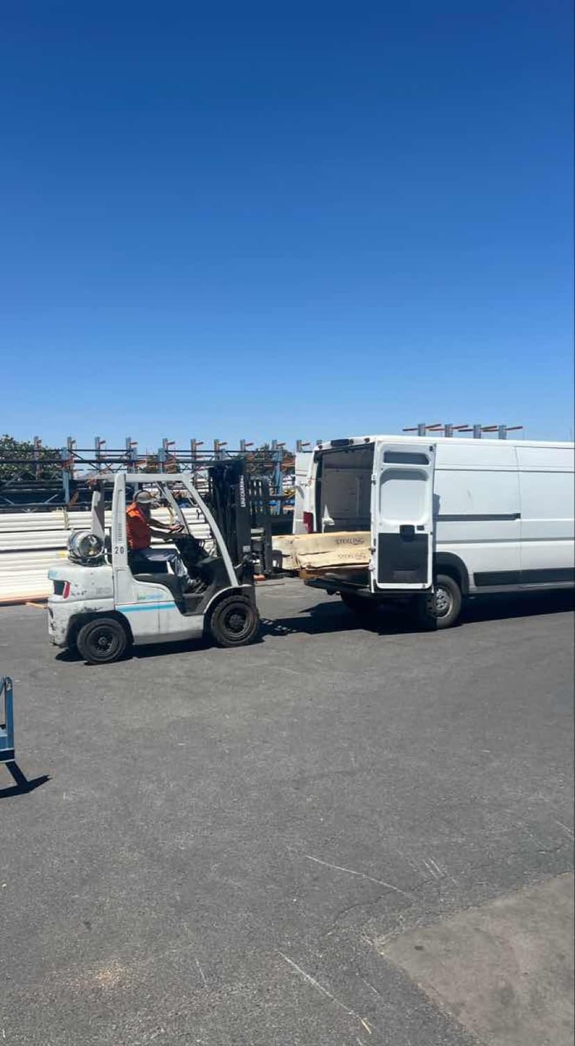 Forklift loading bundled lumber through the rear doors of a white Sprinter Van for a Curri building-supply pickup