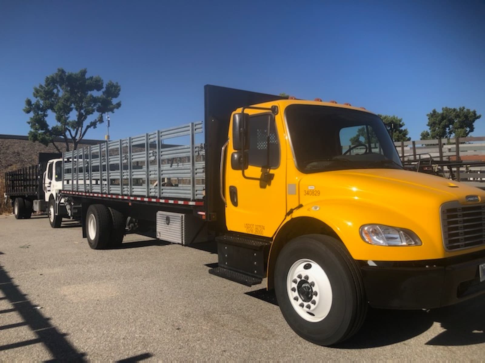 Yellow Curri Freightliner stakebed truck with tall galvanized stake rails along the bed, parked in a sunny lot ready for a same-day open-bed jobsite delivery