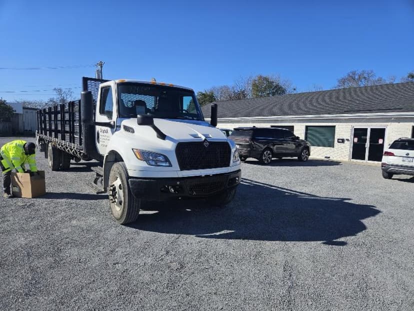 White stakebed truck staged in a parking lot under blue sky with a driver in a safety vest ready for a Curri jobsite delivery
