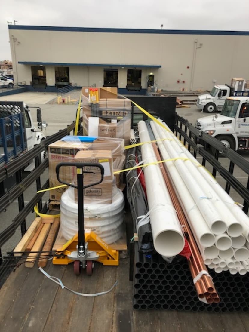 Stakebed loaded with bundles of PVC and copper pipe alongside a pallet jack for a Curri trade-supply delivery