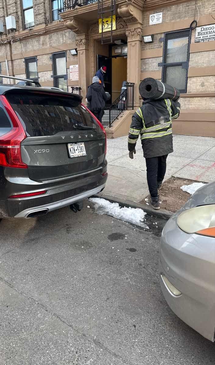 Curri driver carrying a rolled carpet to a Volvo XC90 SUV for a flooring-supply delivery