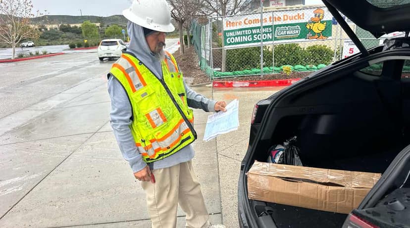 Worker in a hi-vis vest reviewing plans next to an open SUV trunk with cardboard cargo on a Curri jobsite drop-off