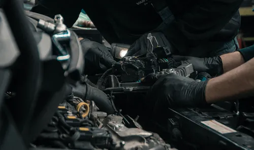 Mechanic in black nitrile gloves reaches into a vehicle engine bay to replace components, the kind of OEM and aftermarket auto parts Curri delivers same-day to shops, dealerships, and parts counters.