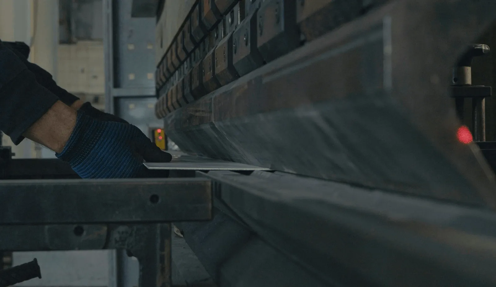 Gloved hand feeds sheet metal into a press brake in a fabrication shop, the kind of industrial work Curri supports with same-day delivery of structural steel, welded assemblies, and MRO supplies.
