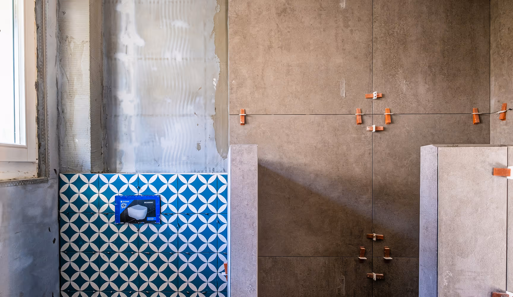 Bathroom under construction with a blue patterned accent tile and gray concrete tile wall, representing the cabinetry, tile, vanities, and fixtures Curri delivers to kitchen and bath showrooms and contractors.