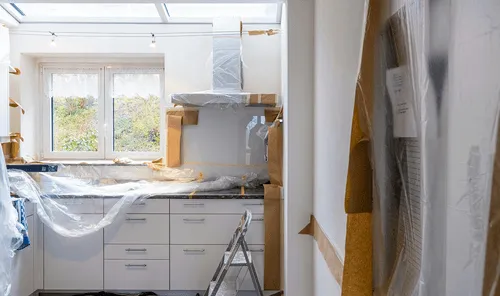Kitchen mid-renovation with plastic sheeting over the counters and new cabinetry lining the wall, the kind of remodel Curri supports with same-day delivery of cabinets, fixtures, countertops, and tile.