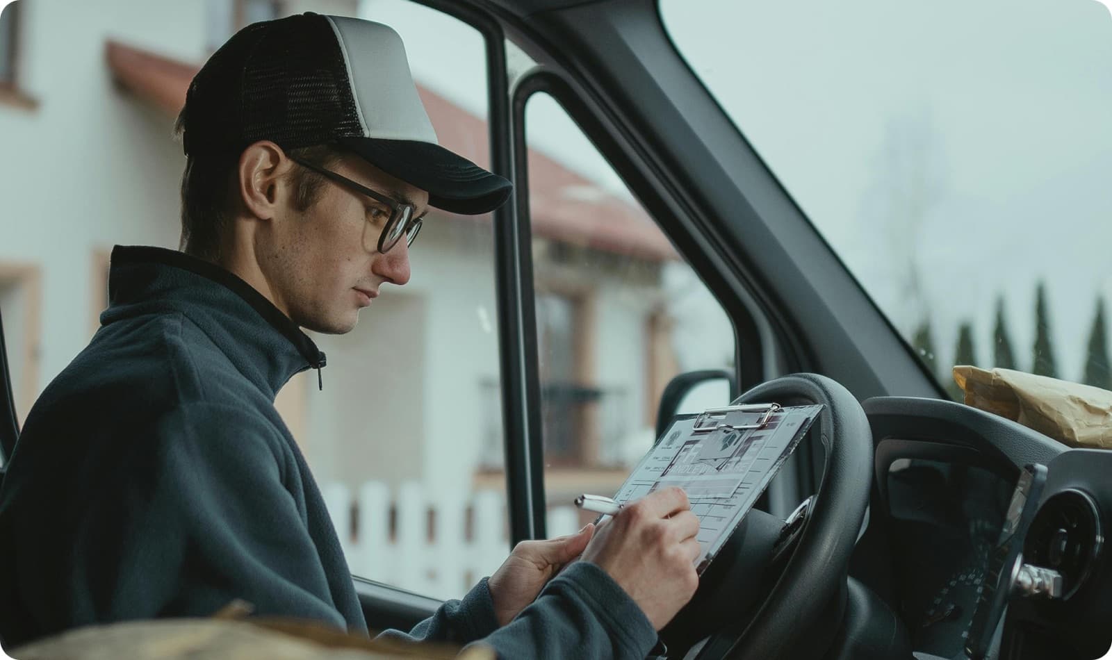 Delivery driver in a cap signs a clipboard inside his van on a medical supply final-mile run, moving PPE, diagnostics, and pharmaceuticals from the distributor to the clinic or hospital door.