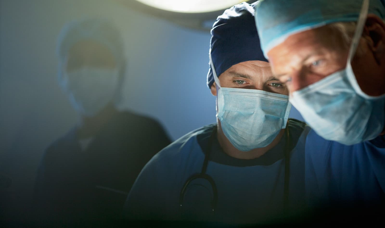 Two surgeons in scrub caps and masks lean over a patient under OR lights in an operating room, the kind of clinical setting Curri supports with compliant same-day delivery of PPE, diagnostics, and pharmaceuticals.