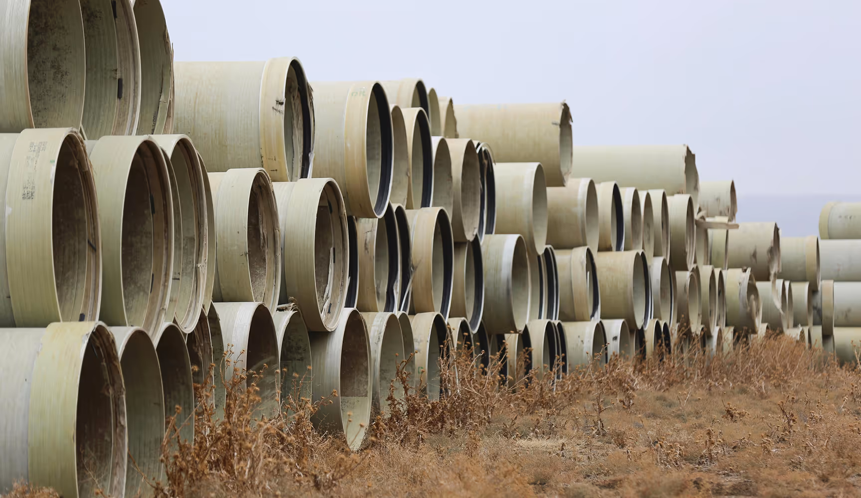 Rows of large-diameter industrial pipe stacked at an outdoor yard, the kind of pipeline and well-site inventory Curri's fleet moves from distributors to oil and gas operators on demand.