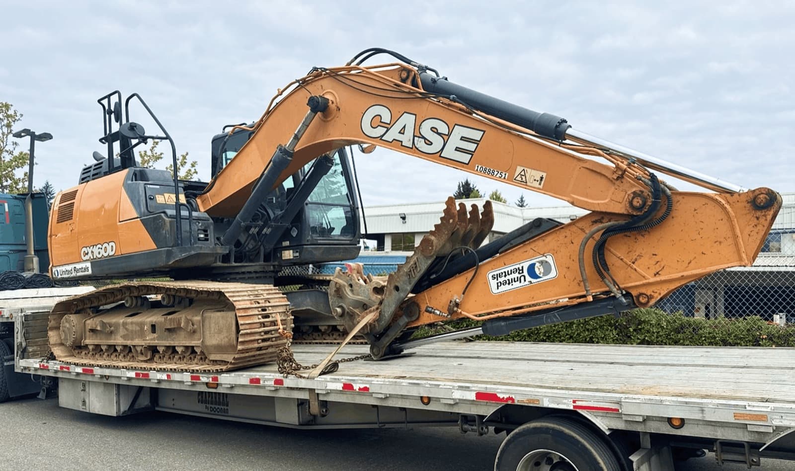 Orange CASE excavator strapped to a United Rentals flatbed trailer ready to ship, representing the aerial lifts, scissor lifts, generators, and compressors Curri moves between rental yards and jobsites.