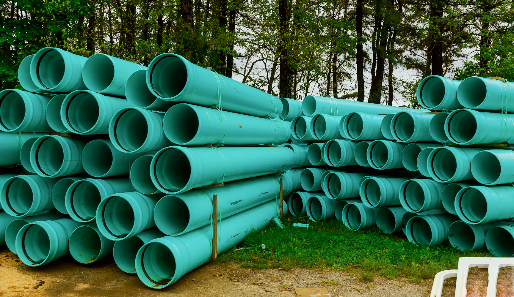 Rows of large green PVC sewer and drainage pipe bundled at an outdoor supply yard, representing the tanks, pumps, and wastewater materials Curri moves for municipal and septic contractors on demand.