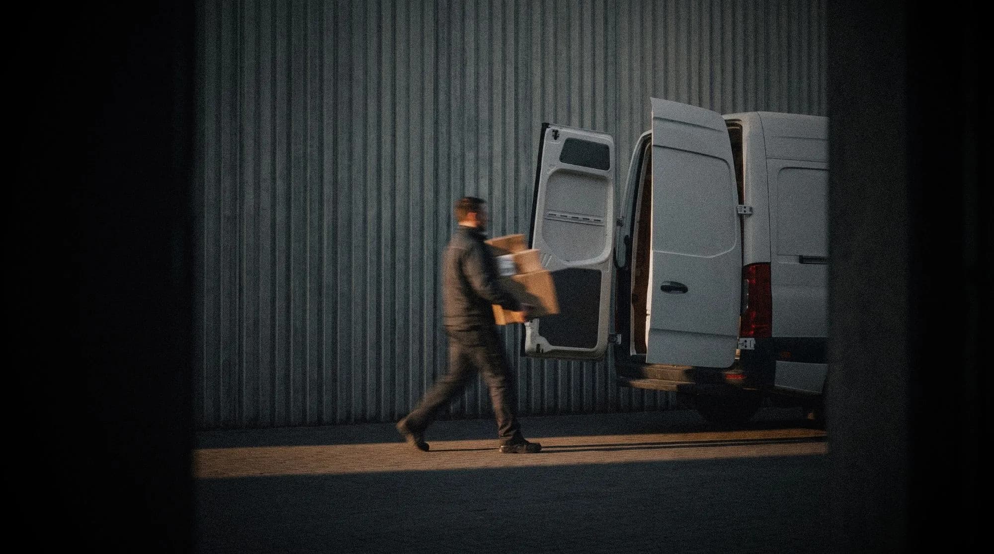 A driver carrying stacked boxes from the open rear doors of a cargo van