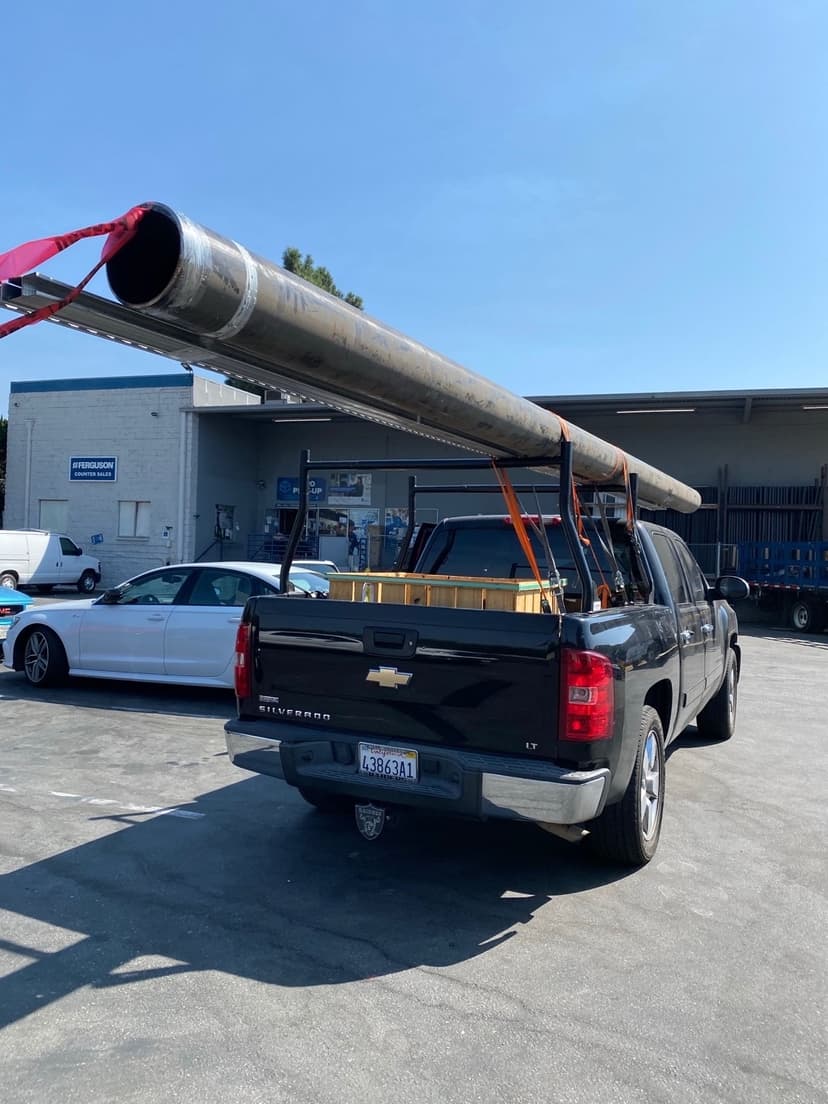 Black Chevy Silverado pickup with overhead pipe rack hauling long black pipe to a Curri jobsite delivery