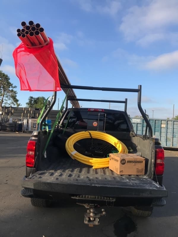 Pickup bed loaded with red PVC pipes in a safety bag and yellow electrical conduit for a Curri trade-supply run