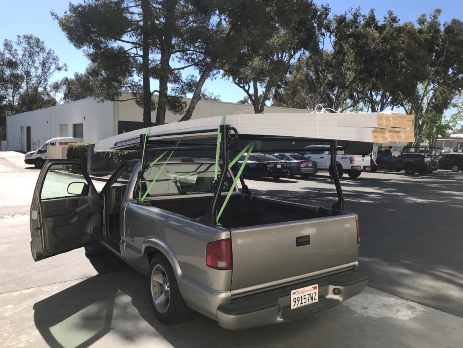 Tan Chevy S-10 pickup carrying flat aluminum panels on its pipe rack for a Curri building-materials delivery