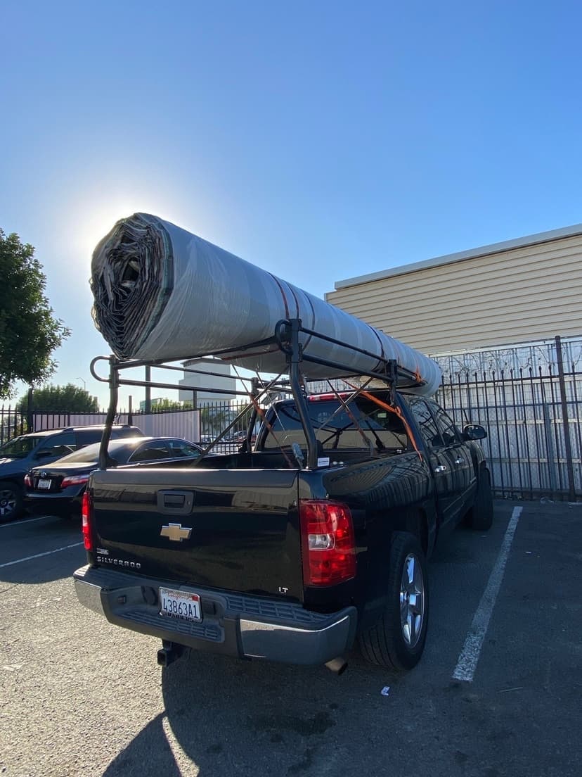 Black Silverado pickup with a wrapped roll of insulation strapped to the pipe rack for a Curri jobsite drop-off