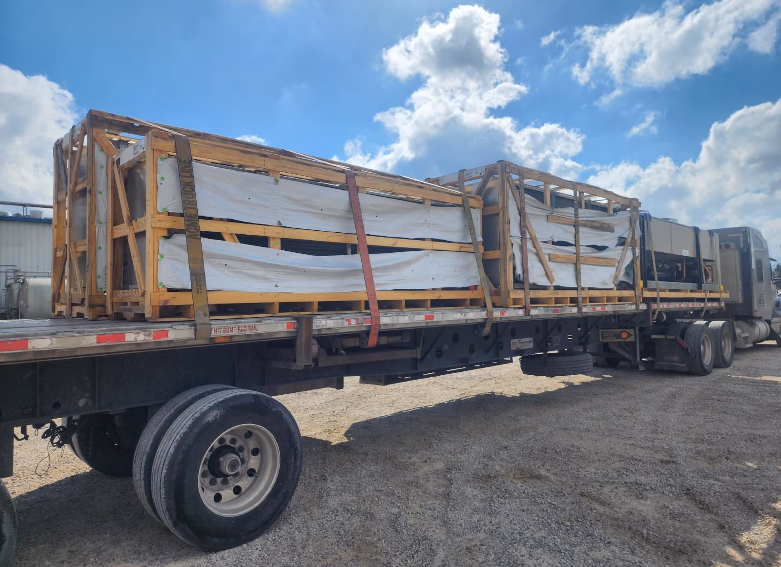 A loaded 53-foot flatbed parked on gravel under open sky, crated freight strapped down across the deck — the kind of run Curri tracks by GPS from the supply house out to the lease.