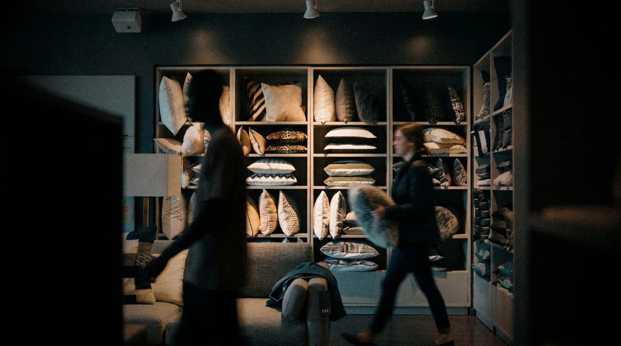 Two people walking past shelves of throw pillows in a furniture showroom